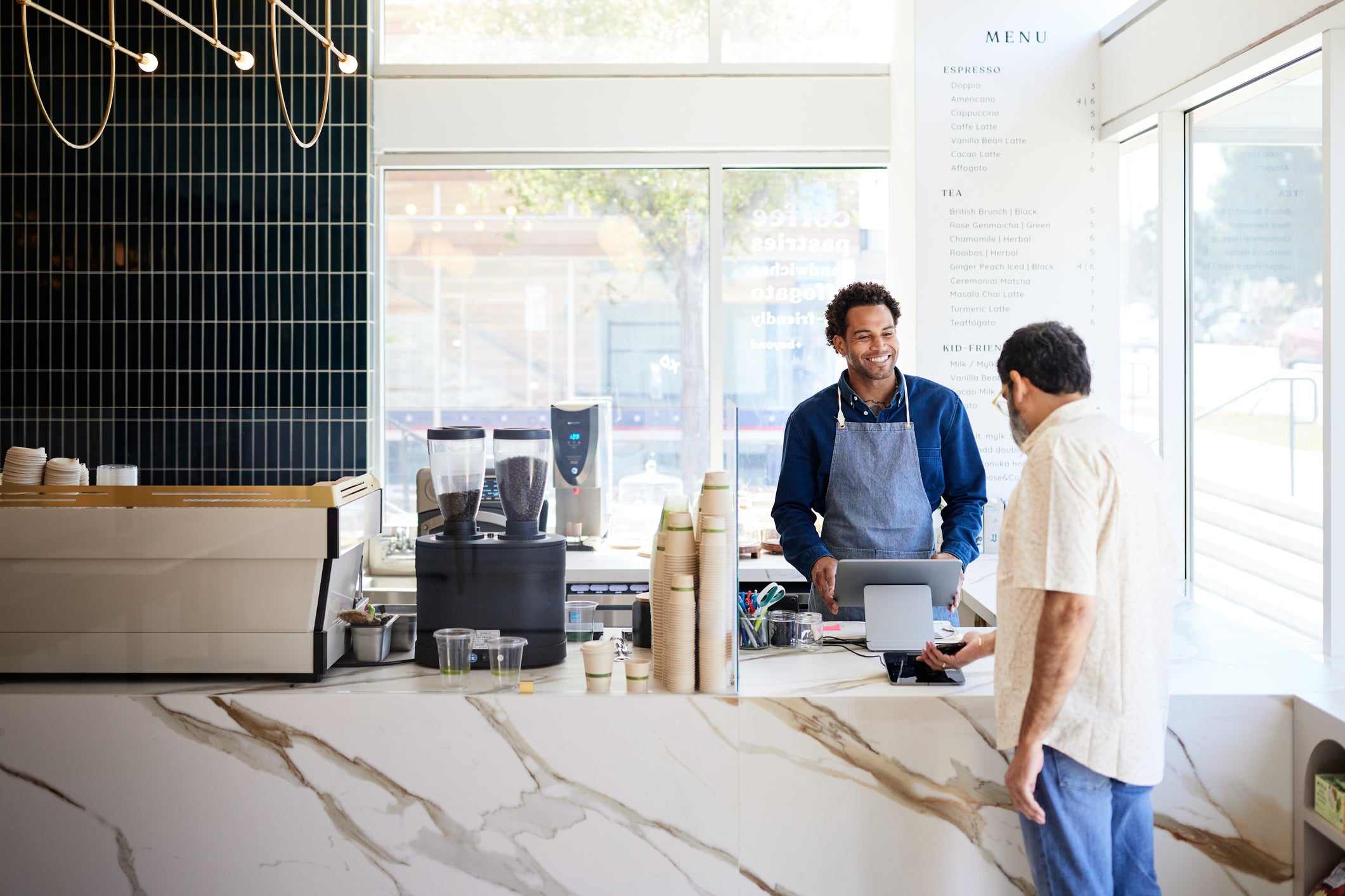 Mature customer doing contactless payment at checkout counter in cafe