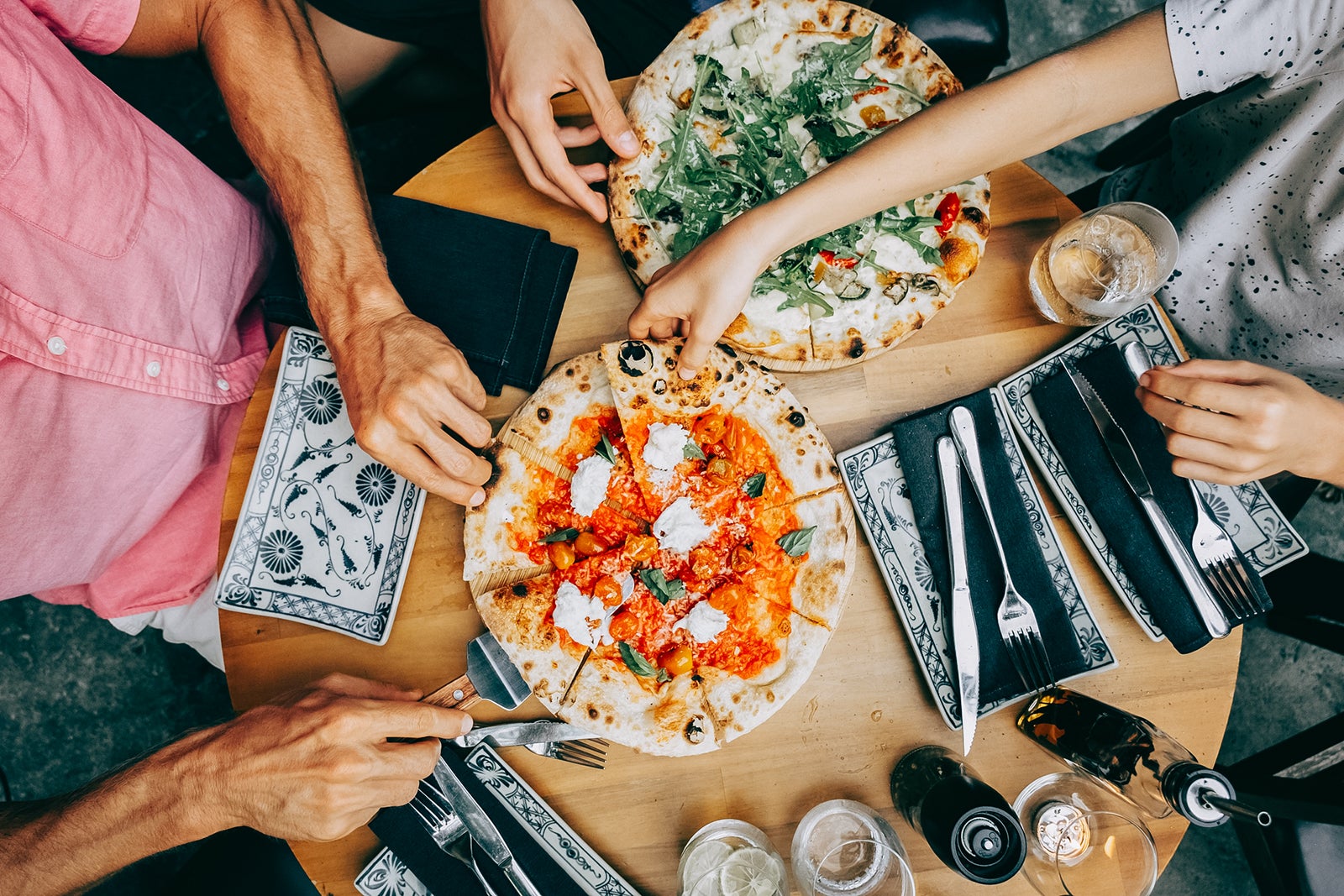 Family sharing pizza at a casual dining table. Hands of friends members reaching for pizza slices at a casual lunch setting.