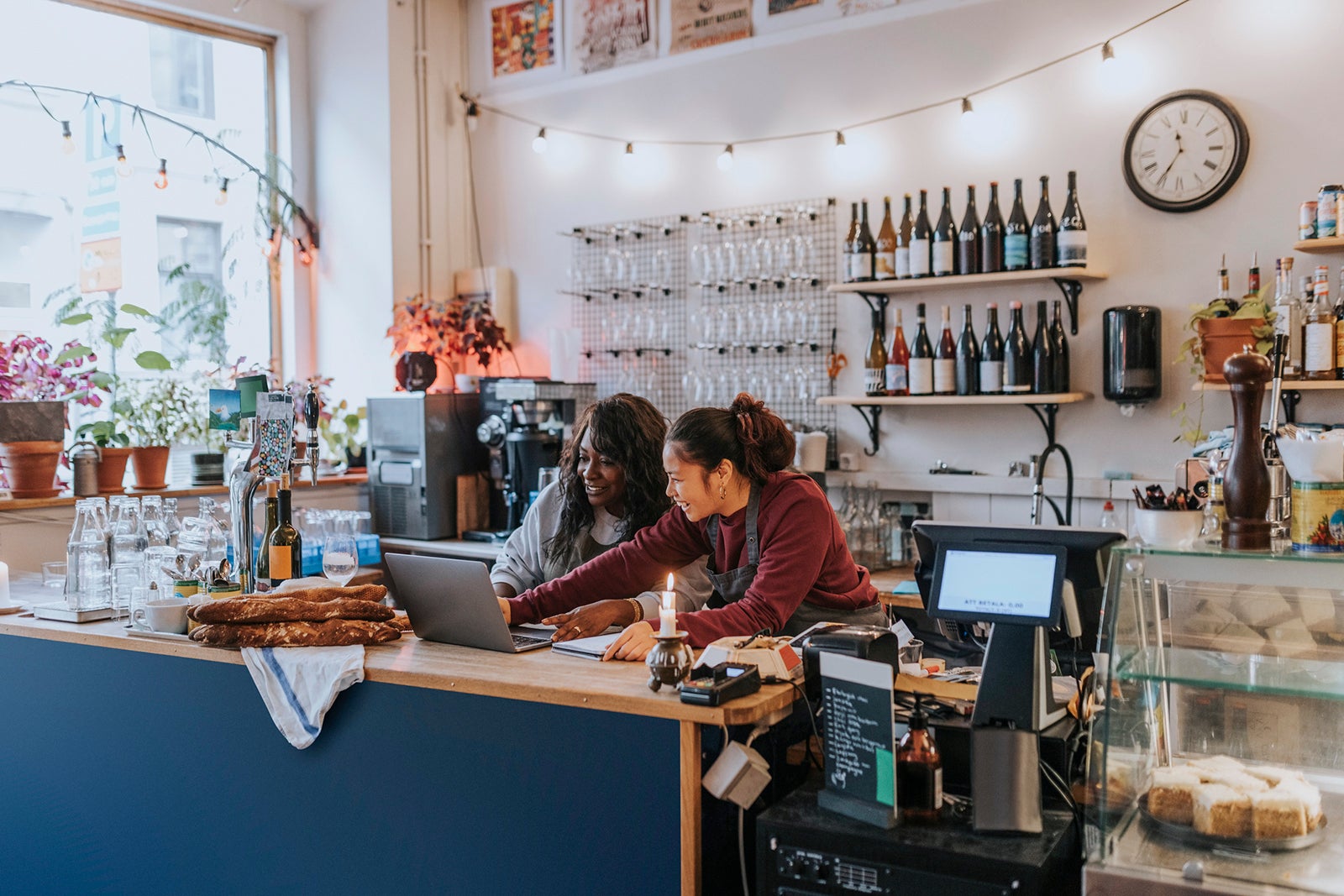 Smiling young female owner discussing over laptop with colleague at checkout in cafe