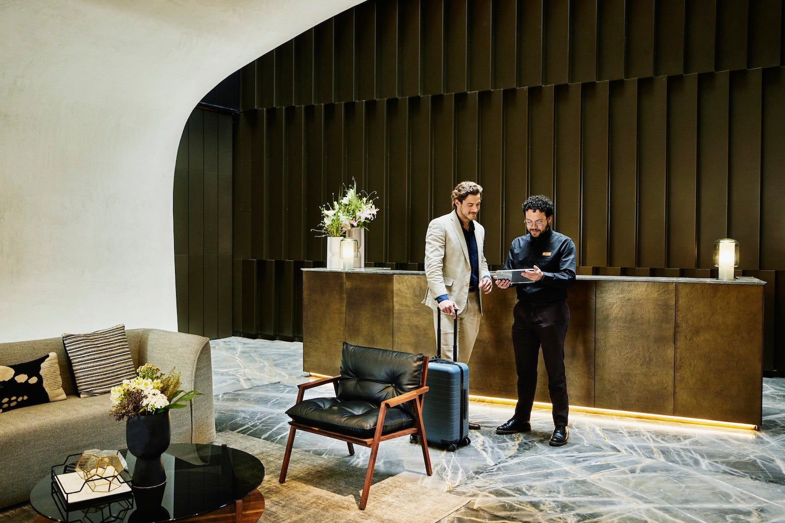 Wide shot manager checking businessman into hotel using digital tablet