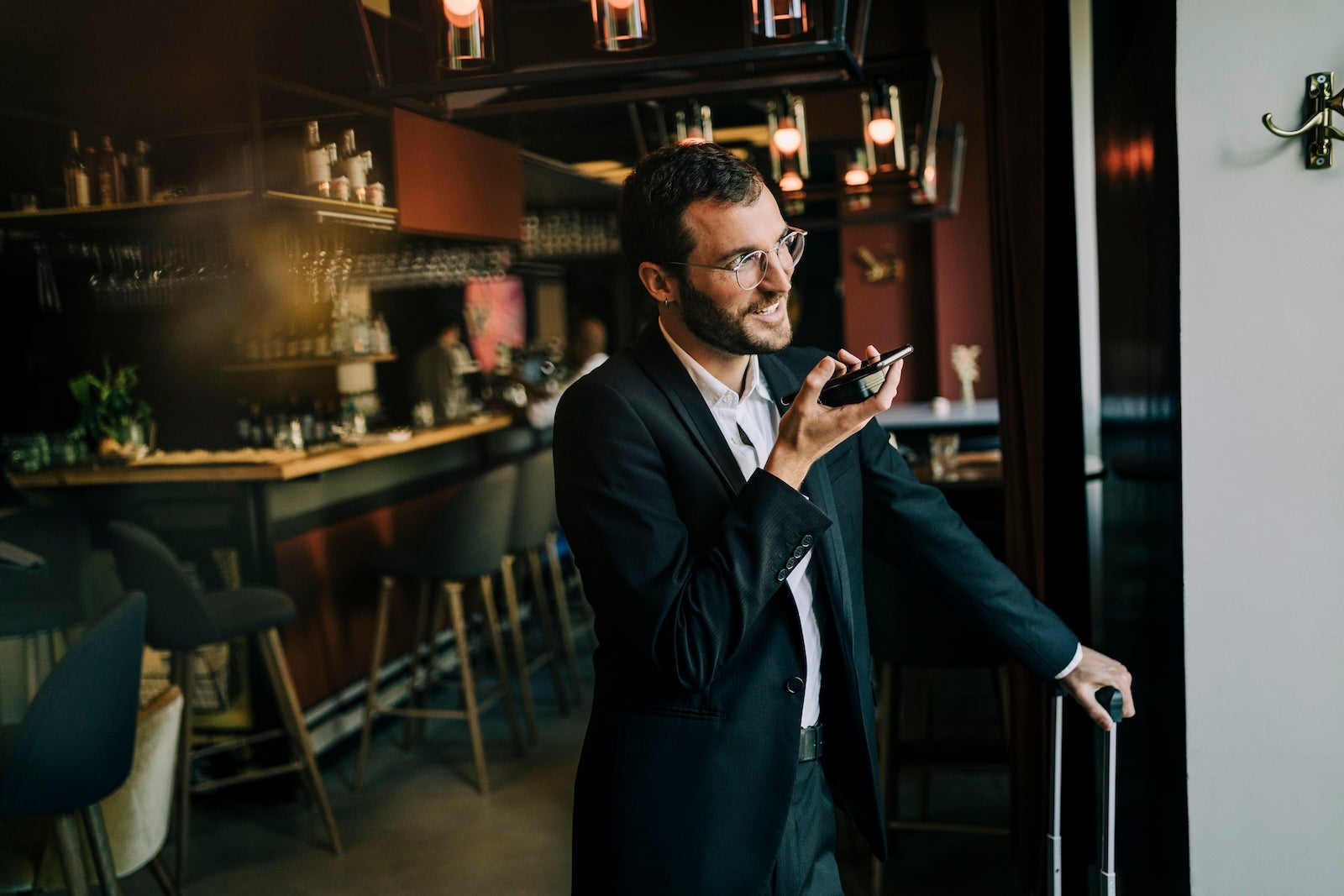 Smiling businessman sending voicemail through smart phone while standing in hotel lobby