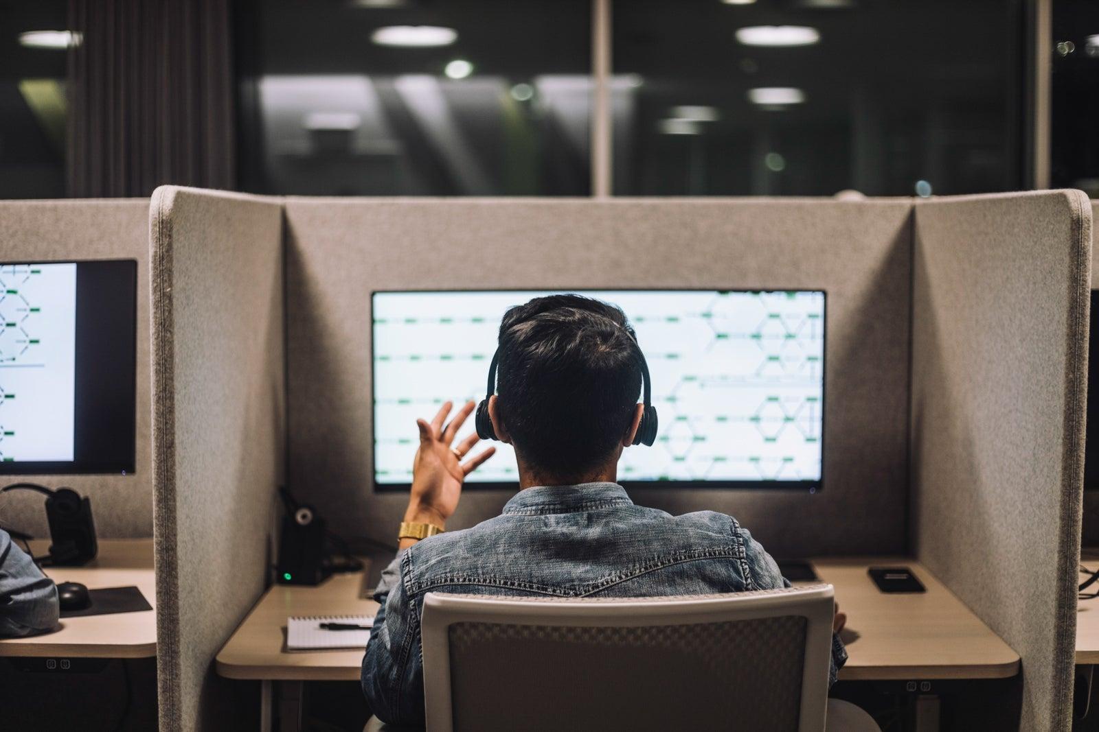 Rear view of young male customer service executive talking through headset sitting at desk in illuminated call center