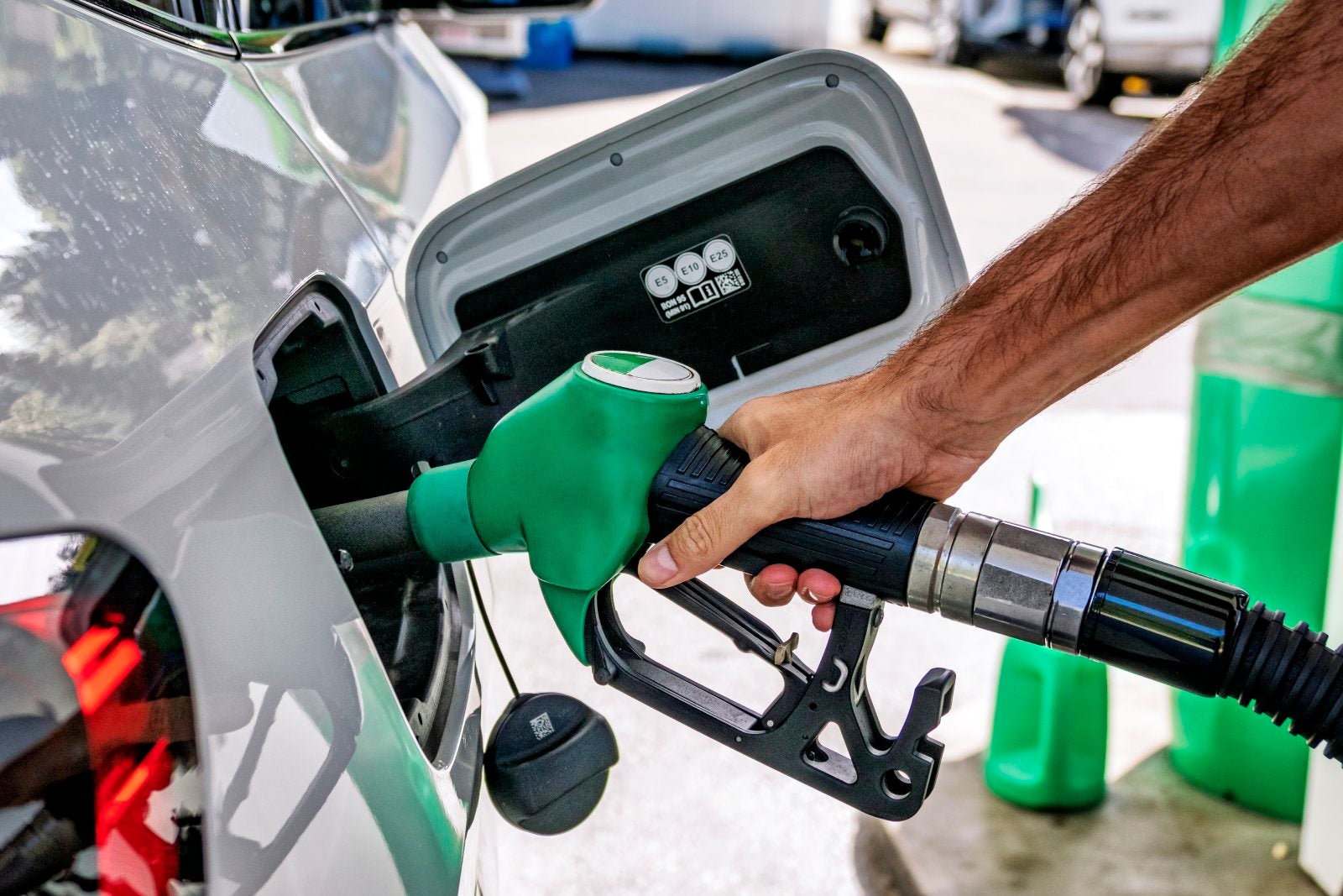 A man's hand holding a fuel hose, refueling an unleaded gasoline vehicle using a self-service pump and hose.